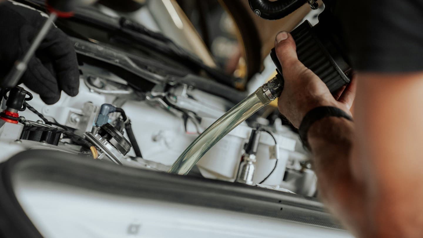 A mechanic servicing the engine bay of a car, fitting a new air filter — the routine maintenance that carries a reliable used car past 200,000 miles