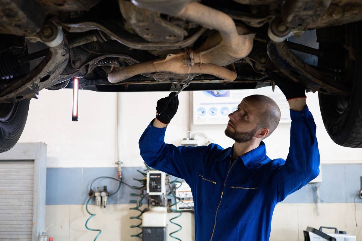 A mechanic in overalls examining the underside of a car raised on a workshop lift